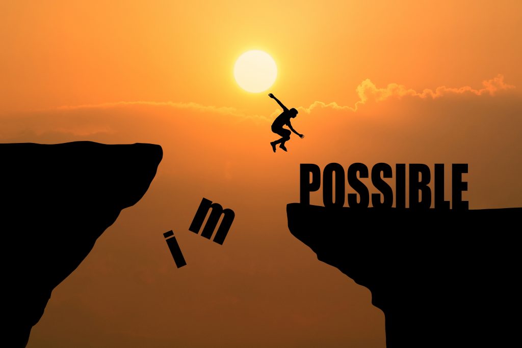 Conscious awakeness: Man jumping over cliff with the words impossible and possible at sunset